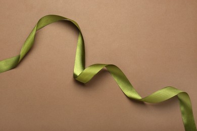 Photo of Beautiful green ribbon on brown background, top view