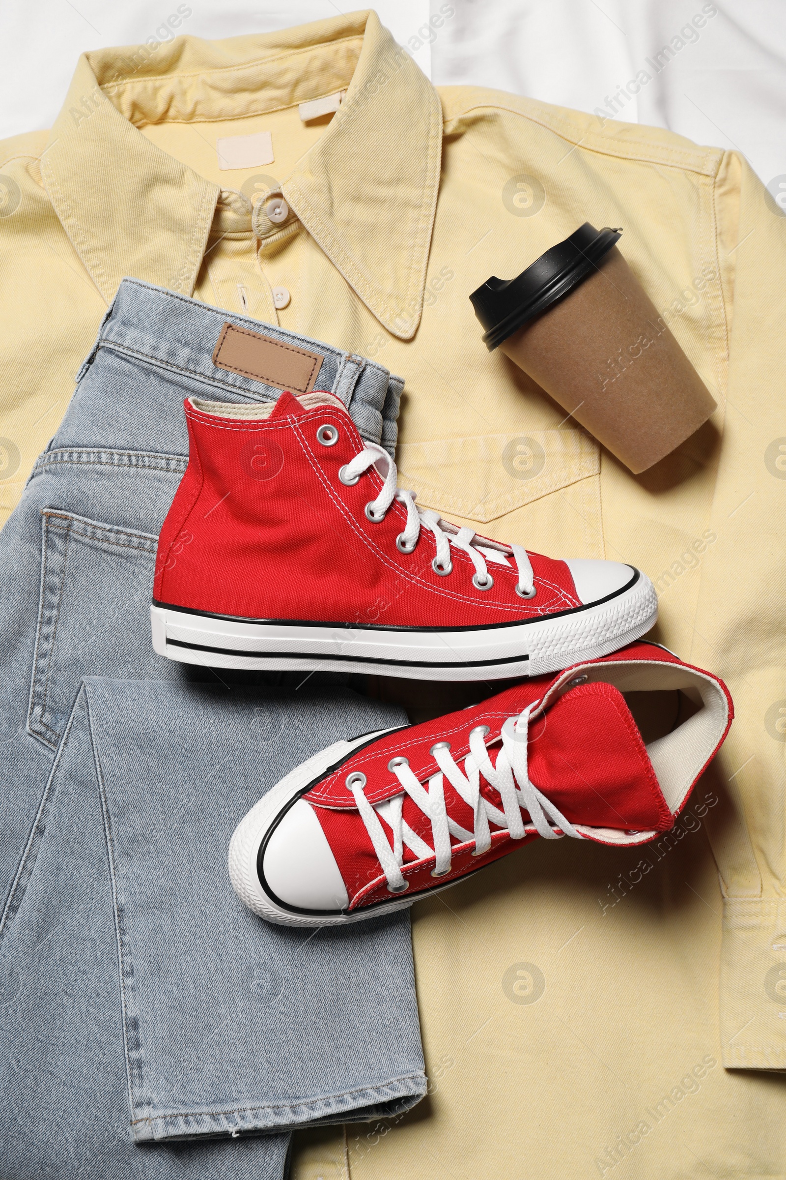 Photo of Pair of stylish red shoes, clothes and paper cup on white fabric, flat lay