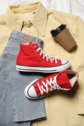 Pair of stylish red shoes, clothes and paper cup on white fabric, flat lay