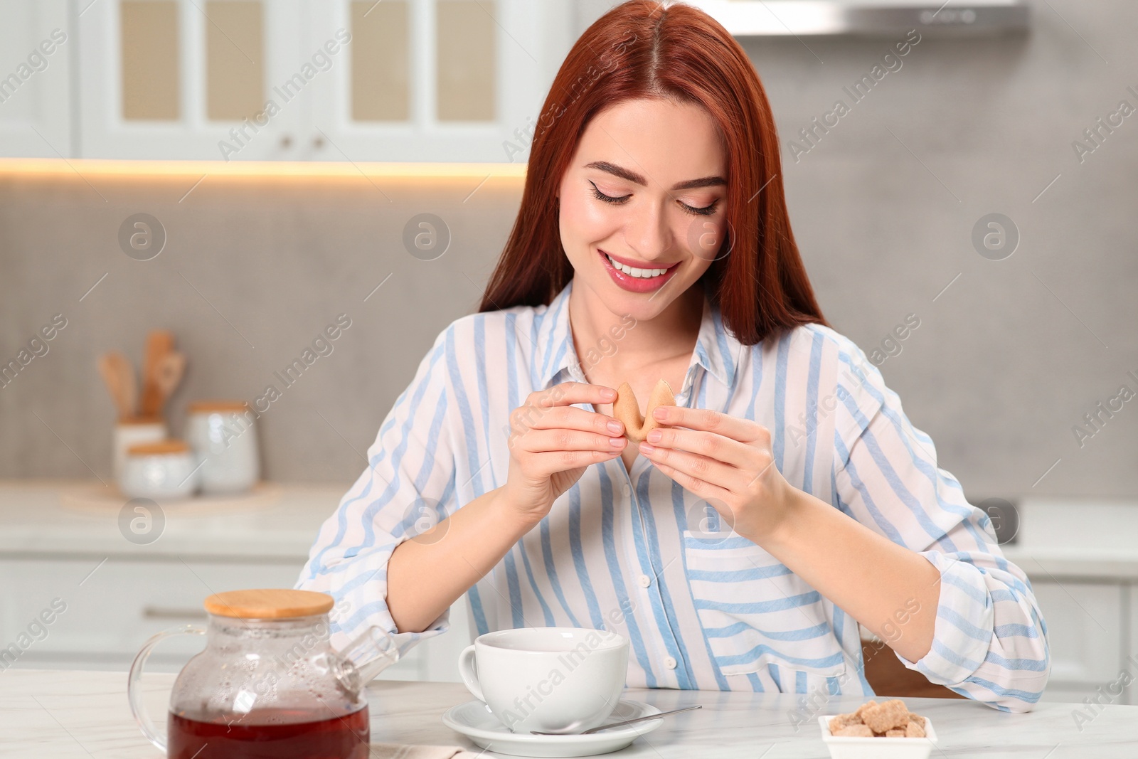 Photo of Happy woman with red dyed hair holding fortune cookie in kitchen