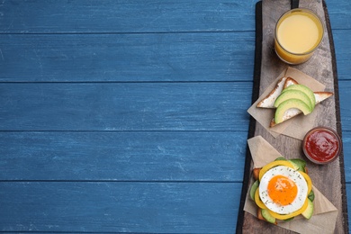 Photo of Tasty toasts with fried egg and avocado served on blue wooden table, top view. Space for text