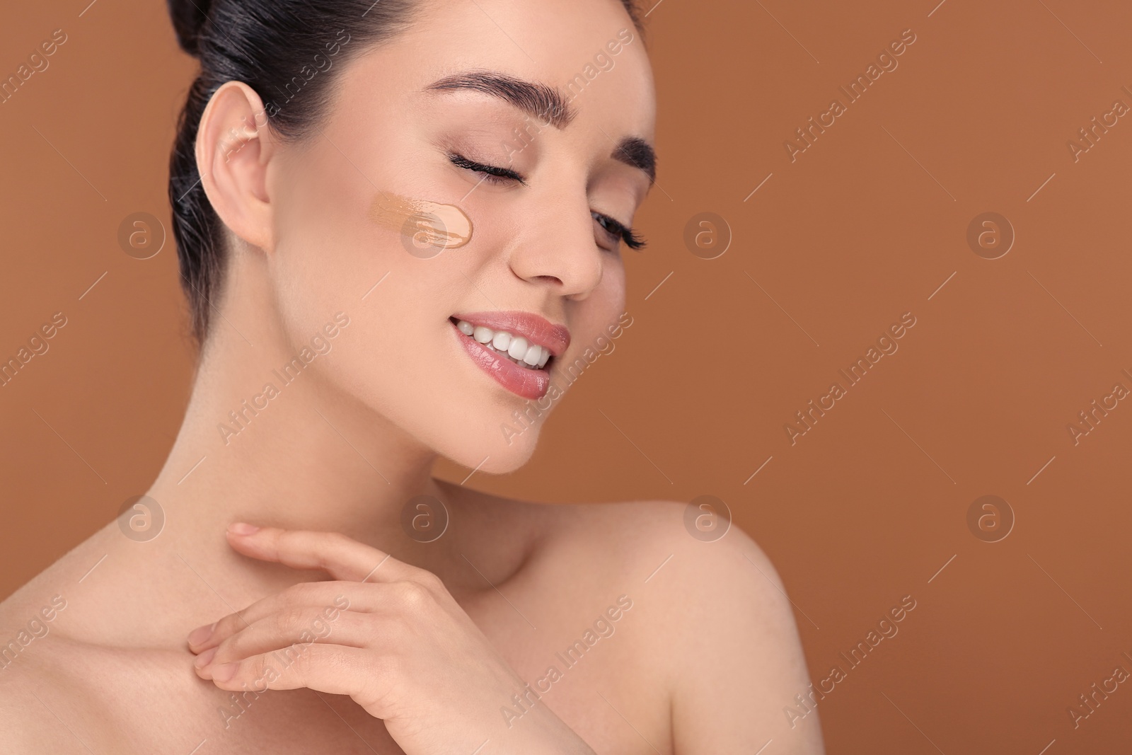 Photo of Woman with swatch of foundation on face against brown background. Space for text