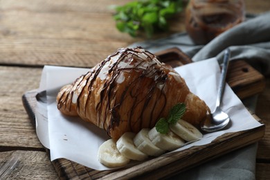 Photo of Delicious croissant with chocolate, banana and spoon on wooden table