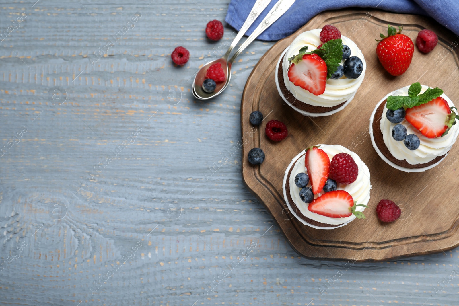 Photo of Sweet cupcakes with fresh berries on wooden table, flat lay. Space for text