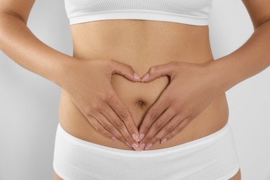 Photo of Woman in underwear making heart with hands on her belly against light background, closeup. Healthy stomach