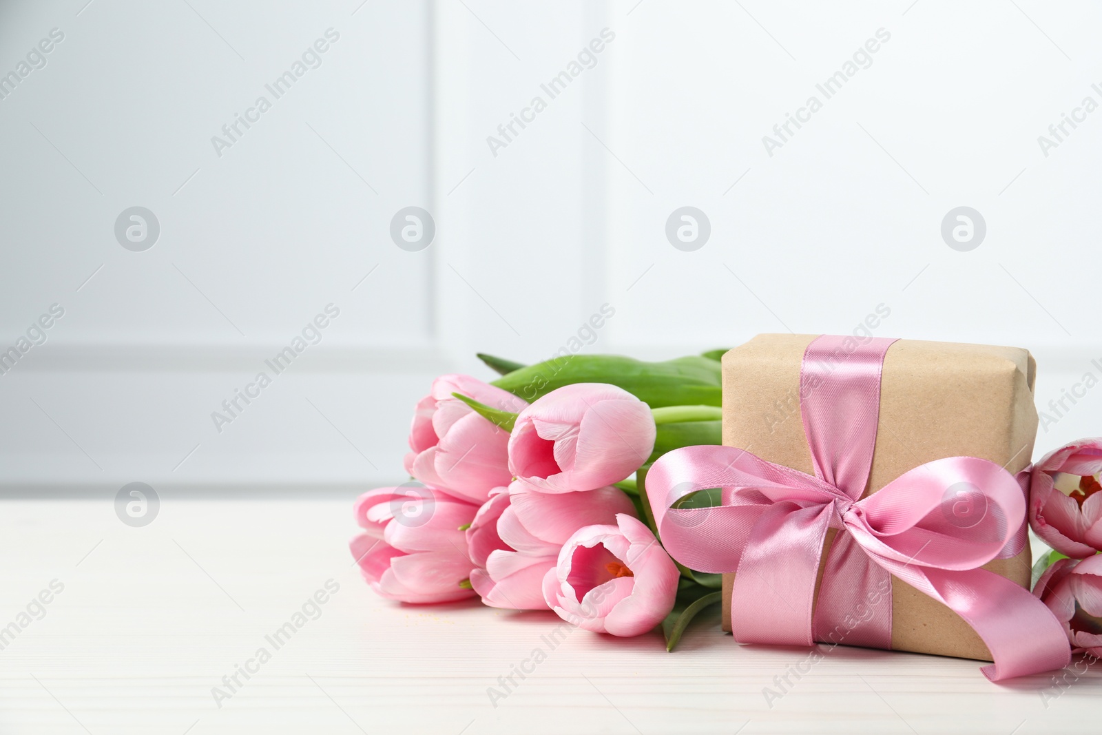 Photo of Beautiful gift box with bow and pink tulips on white table. Space for text