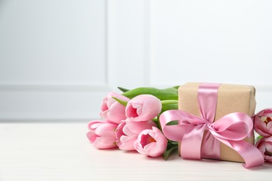 Beautiful gift box with bow and pink tulips on white table. Space for text