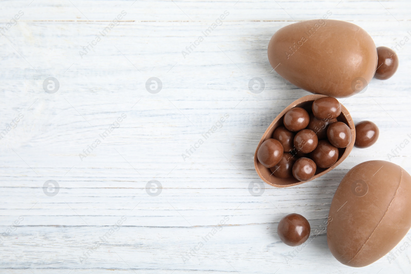 Photo of Whole and broken chocolate eggs with candies on white wooden table, flat lay. Space for text