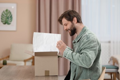 Photo of Happy man opening parcel at home. Internet shopping