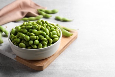 Photo of Bowl of delicious edamame beans on light grey table, space for text