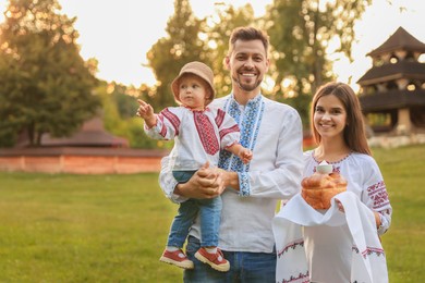 Photo of Happy cute family in embroidered Ukrainian shirts with korovai bread on sunny day. Space for text