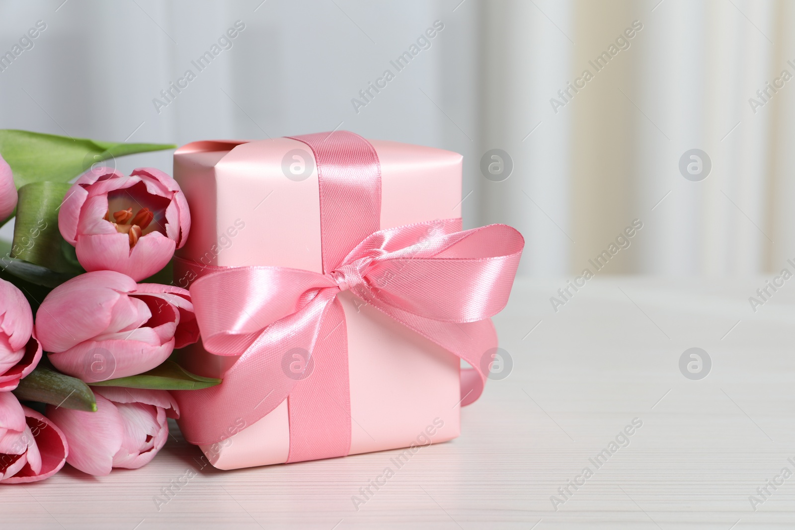 Photo of Beautiful gift box with bow and pink tulip flowers on white table, closeup. Space for text