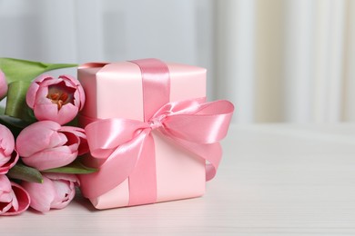 Photo of Beautiful gift box with bow and pink tulip flowers on white table, closeup. Space for text