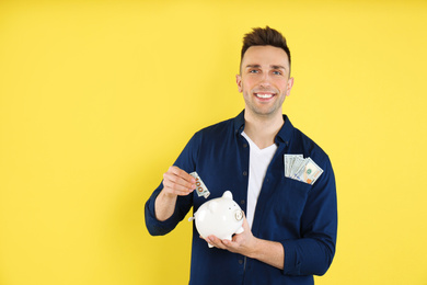 Photo of Happy man putting money into piggybank on yellow background. Space for text