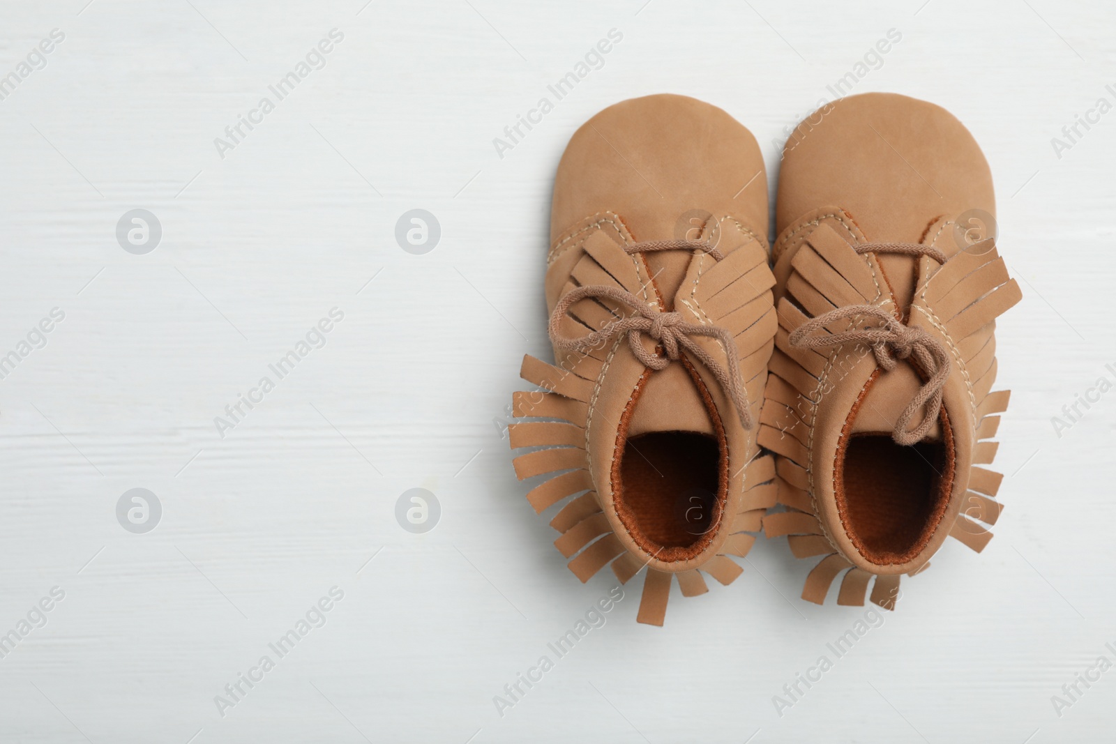 Photo of Top view of child's booties on white wooden background, space for text