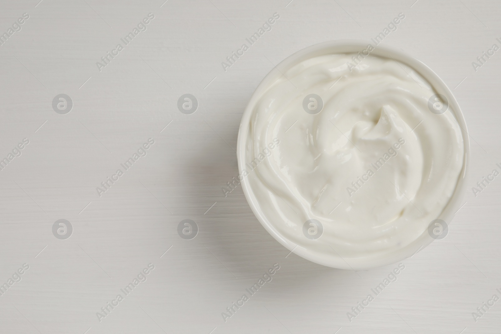 Photo of Bowl of fresh yogurt on white wooden table, top view. Space for text