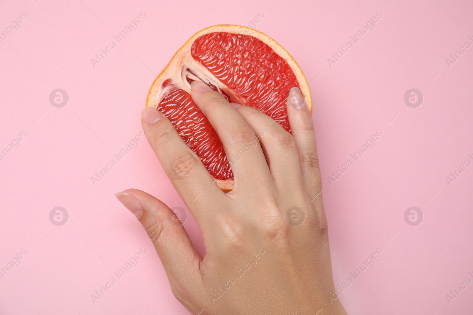 Photo of Young woman touching half of grapefruit on pink background, top view. Sex concept