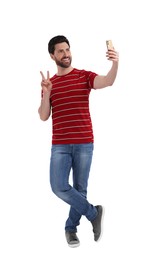 Smiling man taking selfie with smartphone and showing peace sign on white background