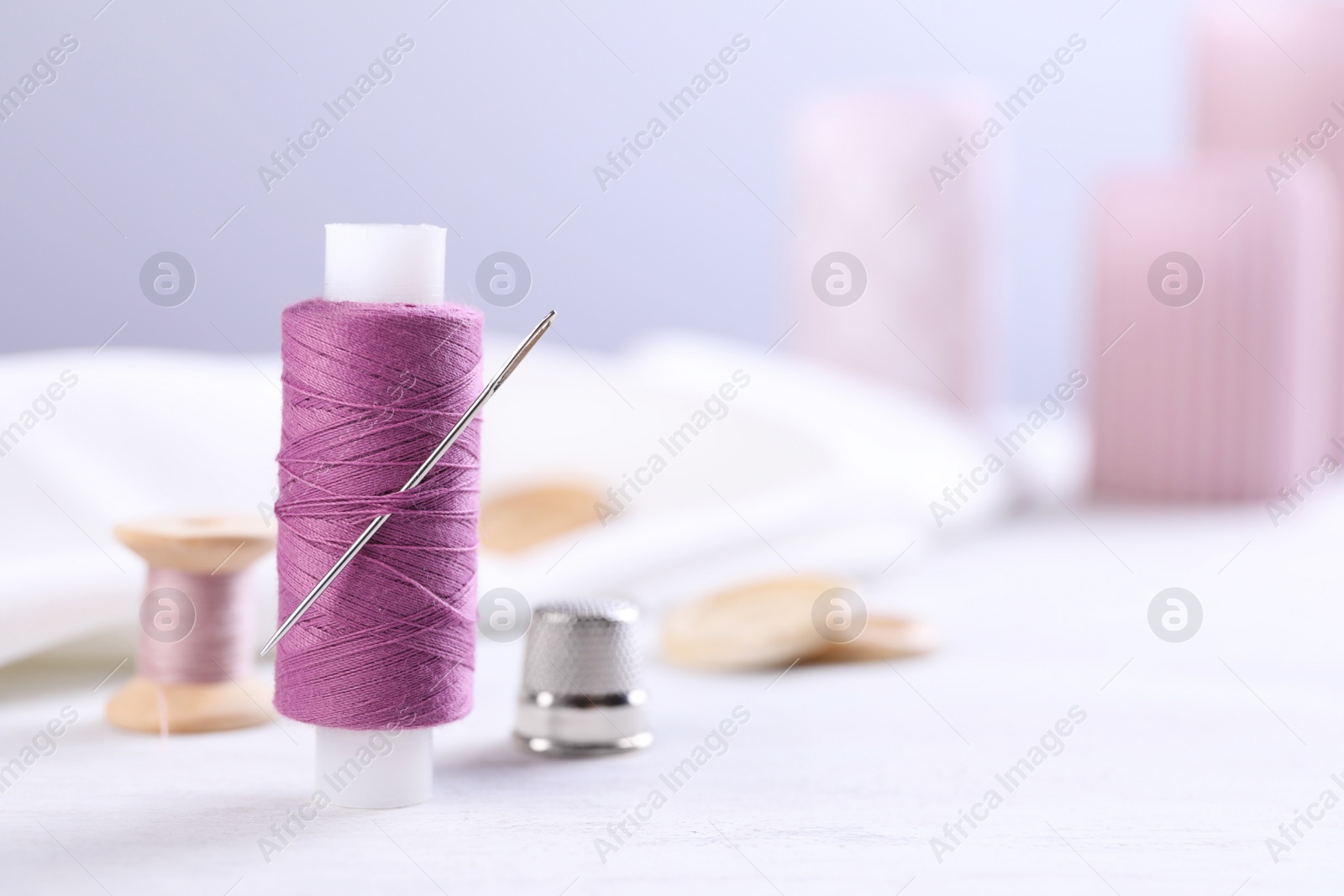 Photo of Spool of purple sewing thread with needle and thimble on white table, space for text