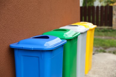 Many colorful recycling bins near brown wall outdoors