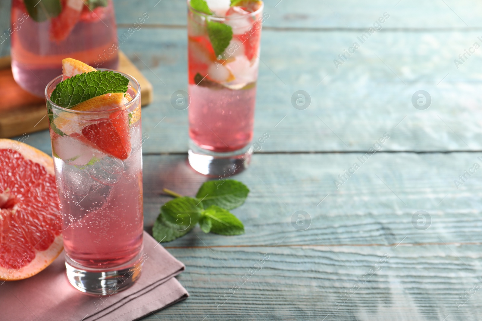 Photo of Delicious grapefruit lemonade with soda water and mint on blue wooden table, space for text. Fresh summer cocktail