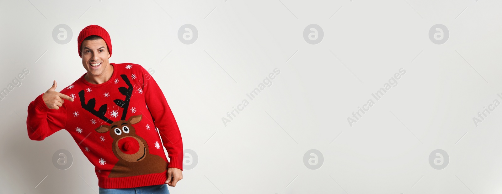 Photo of Happy man in hat pointing on his Christmas sweater against white background, space for text