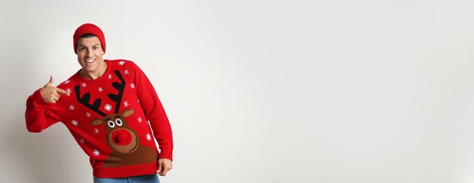 Photo of Happy man in hat pointing on his Christmas sweater against white background, space for text