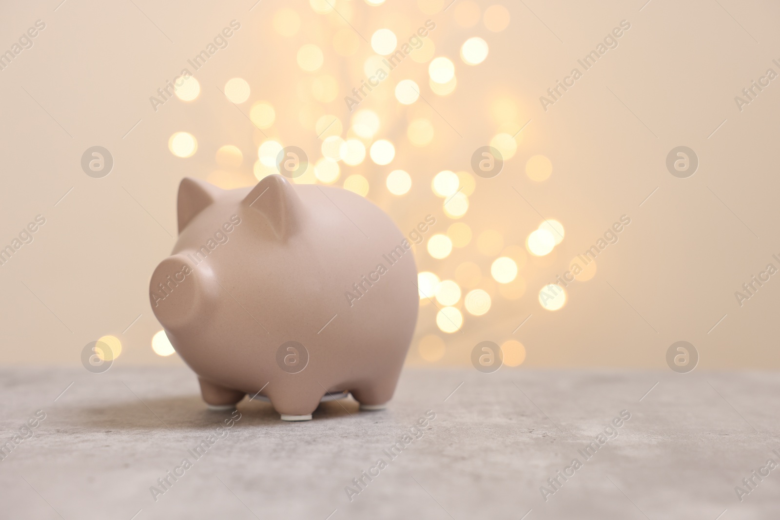 Photo of Piggy bank on grey table against blurred lights, space for text