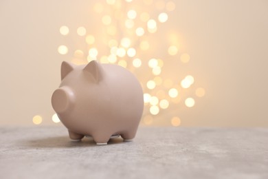 Photo of Piggy bank on grey table against blurred lights, space for text