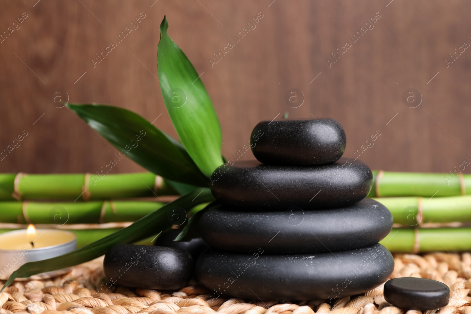 Photo of Stacked spa stones, bamboo and candle on wicker mat, closeup