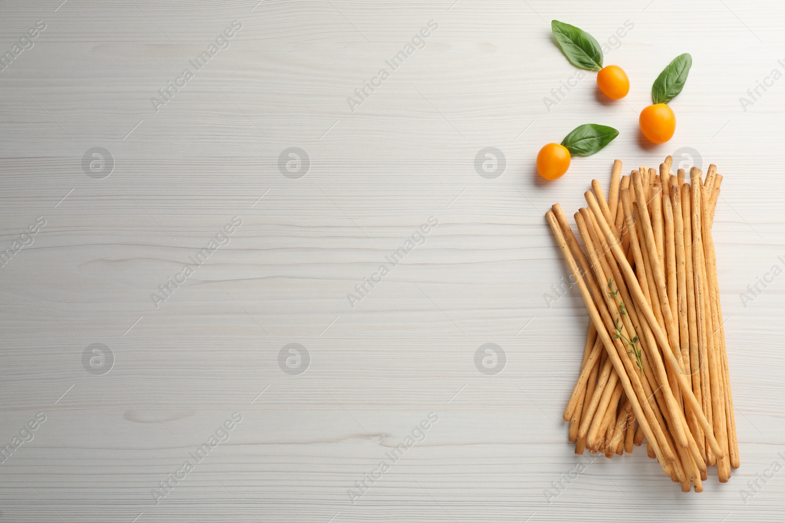 Photo of Delicious grissini sticks, basil leaves and yellow tomatoes on white wooden table, flat lay. Space for text