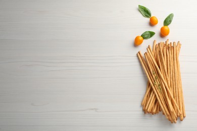 Photo of Delicious grissini sticks, basil leaves and yellow tomatoes on white wooden table, flat lay. Space for text