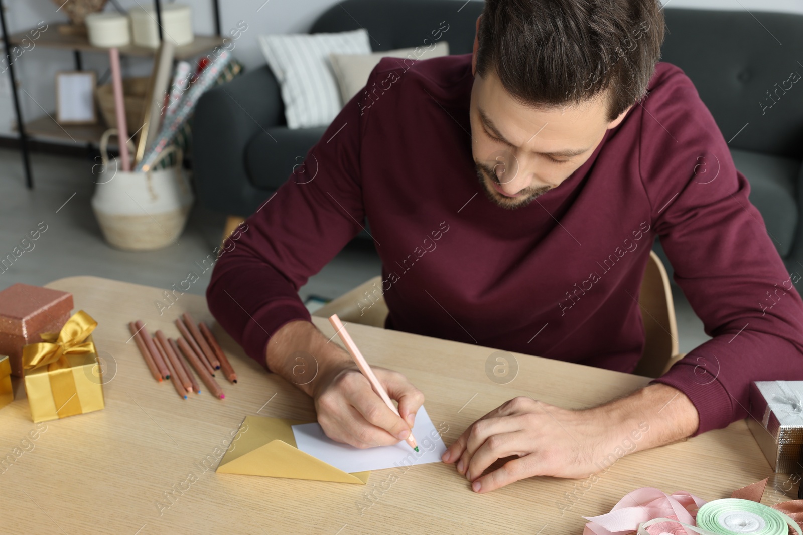 Photo of Man writing message in greeting card at wooden table in room