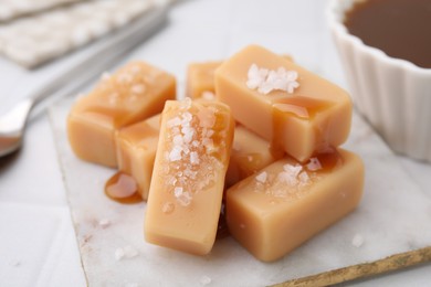 Photo of Delicious candies with sea salt and caramel sauce on white tiled table, closeup