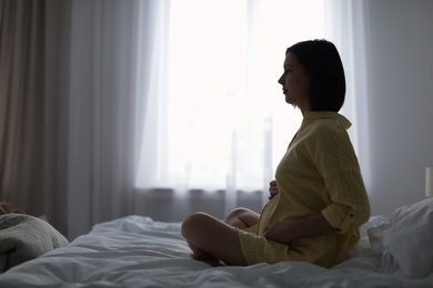 Beautiful pregnant woman sitting on bed at home. Space for text