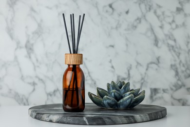 Air reed freshener and ceramic decor on table near marble wall. Space for text