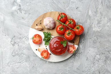 Photo of Delicious ketchup in bowl, parsley, garlic and tomatoes on grey textured table, top view