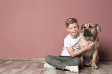 Cute little child with his dog sitting on floor near color wall