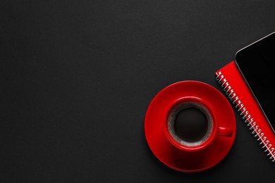 Photo of Red cup with aromatic coffee and notepads on black background, flat lay. Space for text