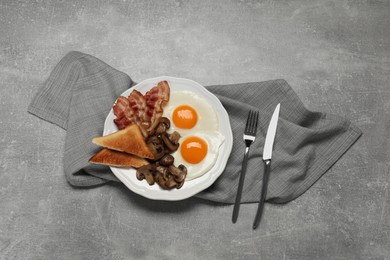 Plate with fried eggs, mushrooms, bacon and toasted bread on grey table, flat lay. Traditional English breakfast
