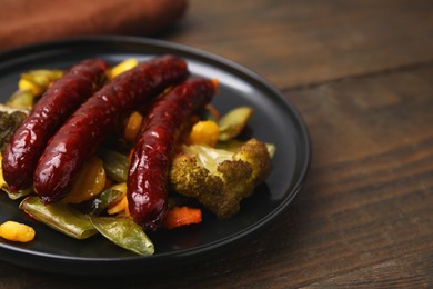 Photo of Delicious smoked sausages and baked vegetables on wooden table, closeup