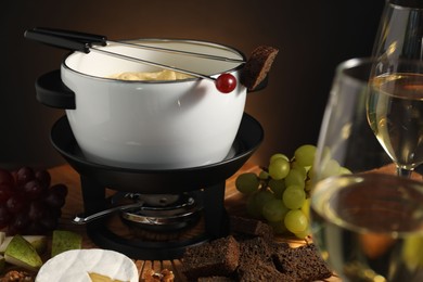 Photo of Forks with pieces of grape, bread, fondue pot with melted cheese, wine and snacks on table, closeup