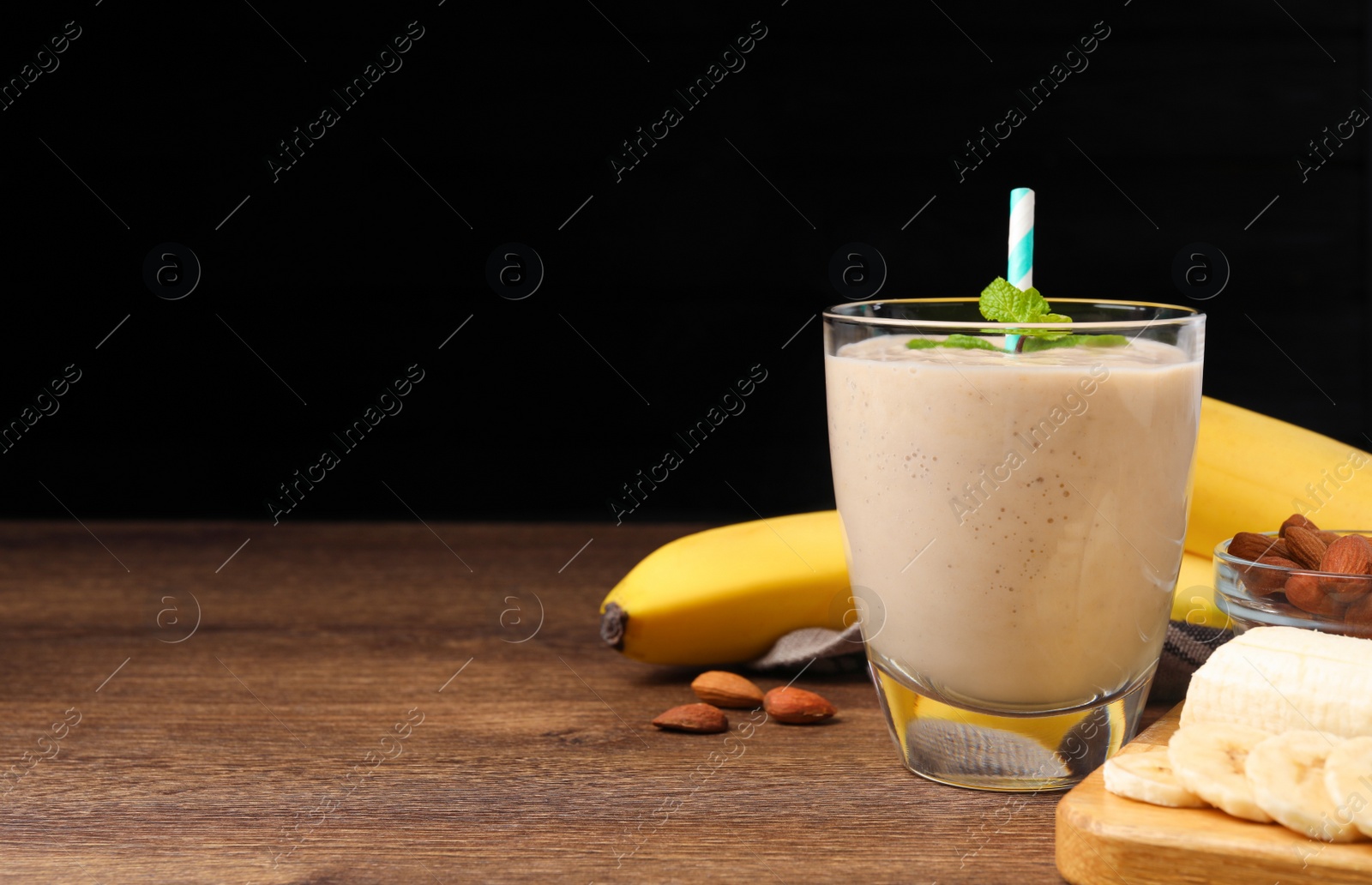 Photo of Glass with banana smoothie and mint on wooden table against black background. Space for text