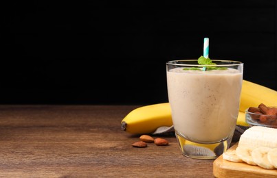 Glass with banana smoothie and mint on wooden table against black background. Space for text