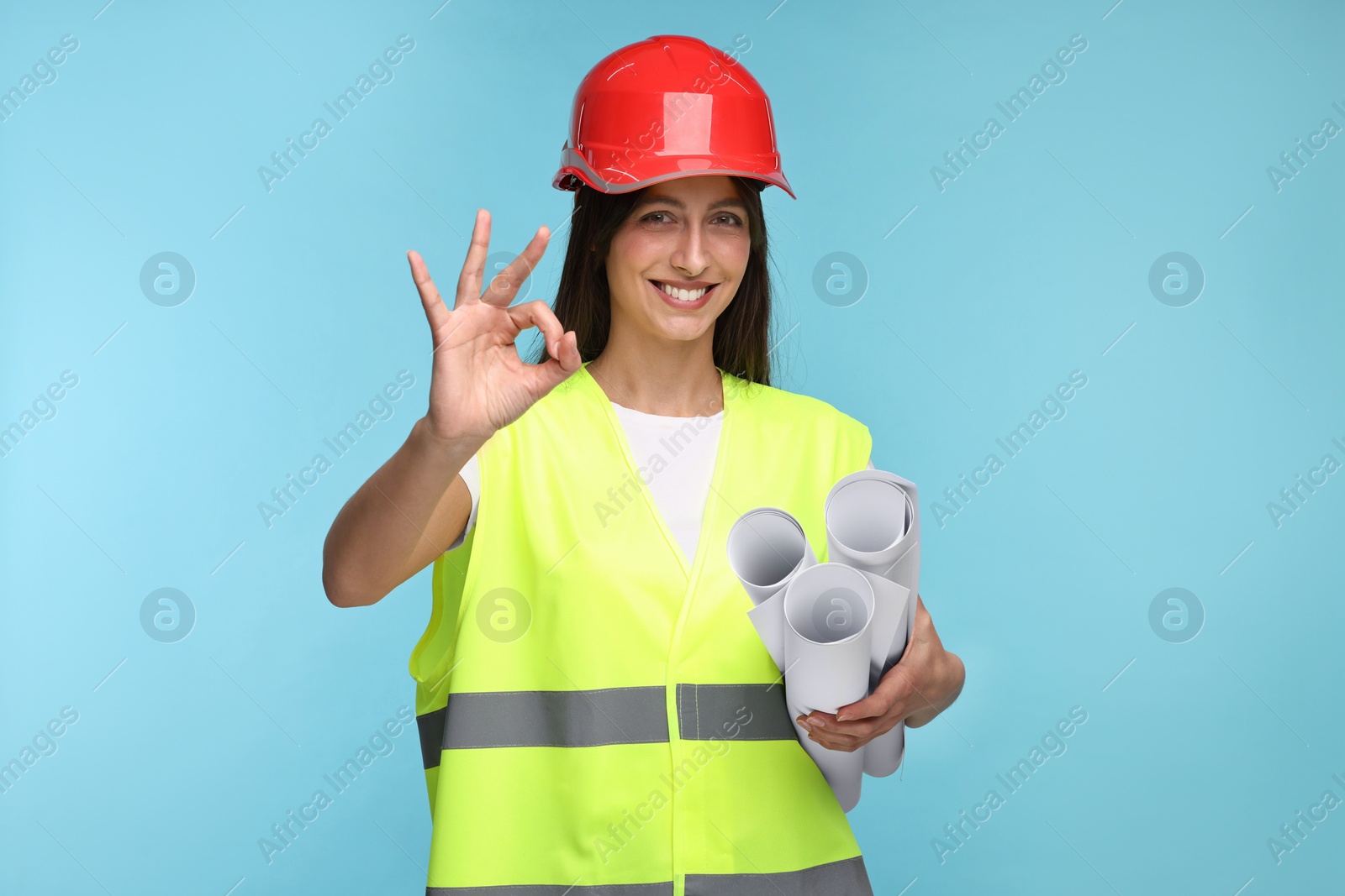 Photo of Architect in hard hat with drafts showing ok gesture on light blue background