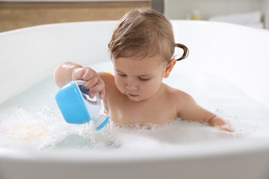 Photo of Cute little girl playing in foamy bath at home