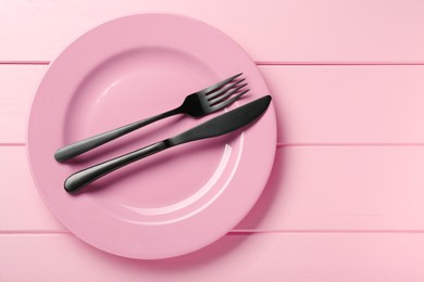 Ceramic plate with cutlery on pink wooden table, top view. Space for text