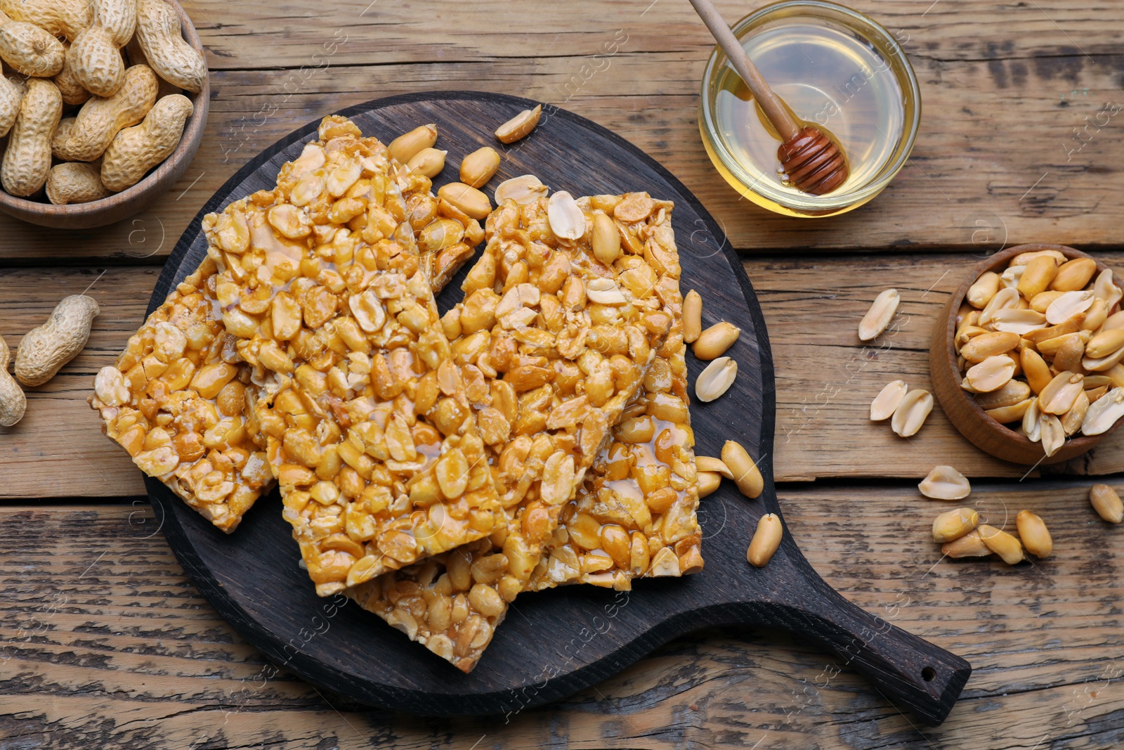 Photo of Delicious peanut kozinaki bars, nuts and honey on wooden table, flat lay