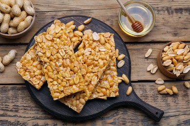 Photo of Delicious peanut kozinaki bars, nuts and honey on wooden table, flat lay