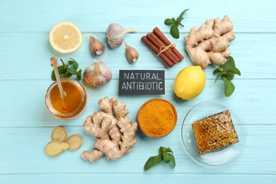 Different fresh products and card with phrase Natural Antibiotic on light blue wooden background, flat lay